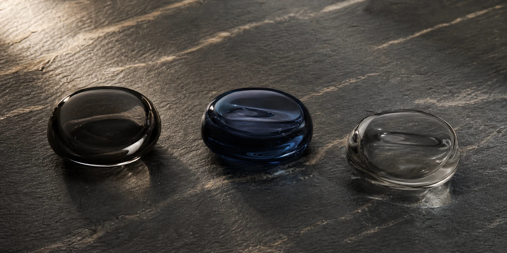 Three equal charcoal and slate glass forms representing the verified KLAPP Men catalogue records in Finland.