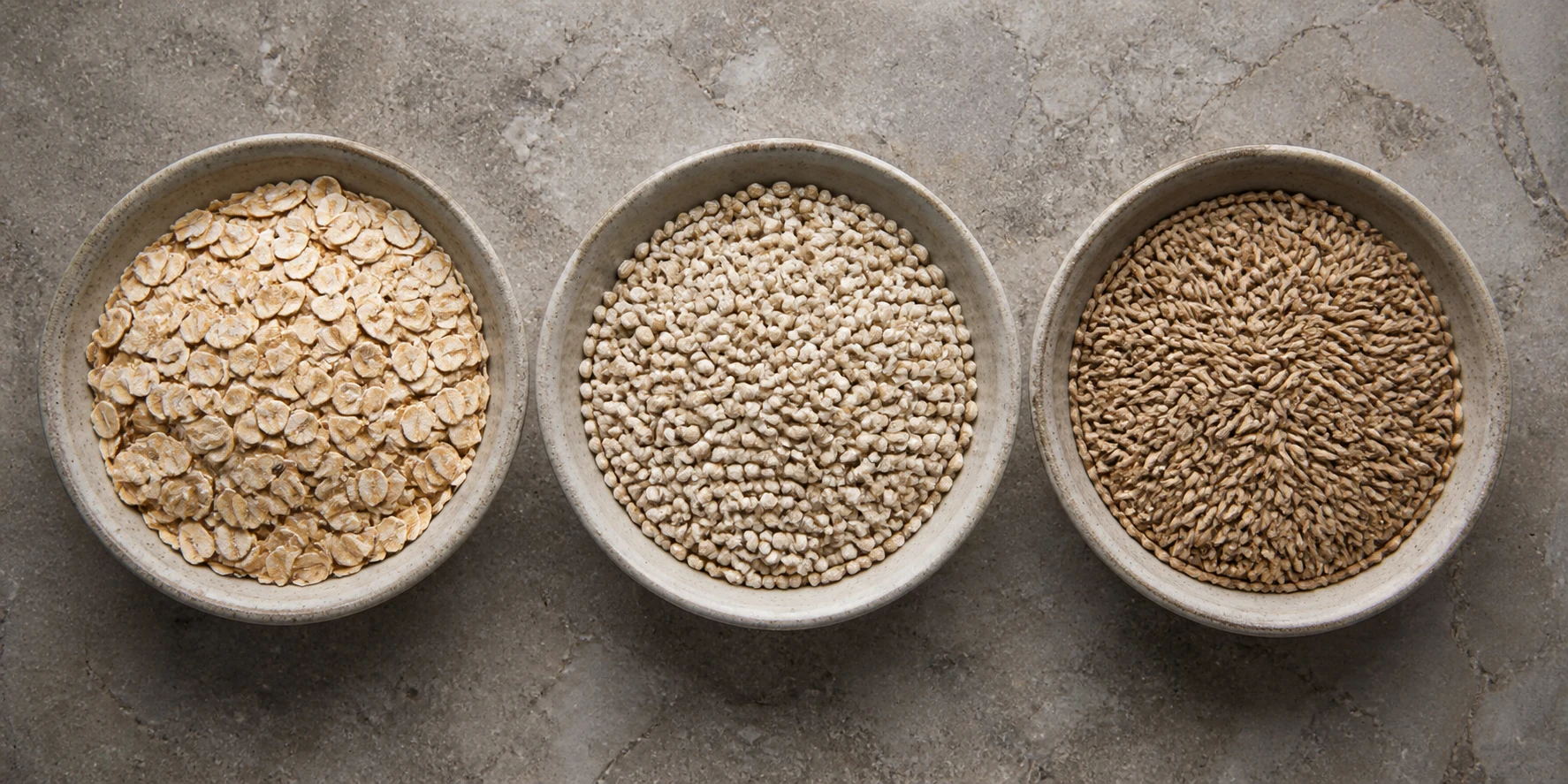 Three equal bowls of oats, barley and rye arranged for a neutral GI-comparison guide.
